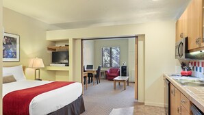 A hotel room with a bed, a desk, a chair, a TV, a kitchen area with a sink and cabinets, and a window with a view of trees. - 250 | Easy-Breezy Studio -AC, Spas, Pool & Tennis (Olympic Valley)