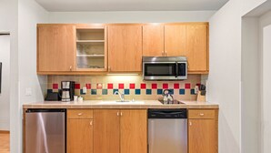 Una cocina compacta con armarios de madera, lavavajillas de acero inoxidable, microondas y salpicadero de azulejos.