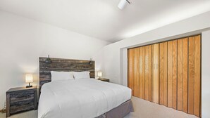 Un dormitorio con una cama grande, cabecera de madera, dos mesitas de noche con lámparas y un armario de madera.