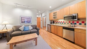 Un apartamento moderno con kitchenette, un sofá gris, una mesa de centro de madera y un cuadro en la pared.