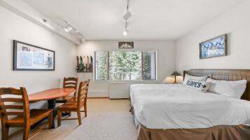 A bedroom with a bed, a desk, chairs, and a window with blinds.