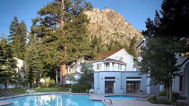 A swimming pool with a mountain backdrop, surrounded by trees and a building with a white facade.