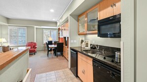 A compact kitchen with a microwave, stove, and dishwasher. There is a dining area with a table and chairs, and a red chair.