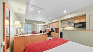 A compact hotel room with a bed, a desk, a kitchenette, and a bathroom.