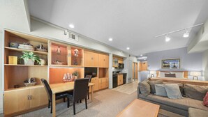 A modern living room with a sofa, a dining table, and a kitchen area with wooden cabinets and a microwave.