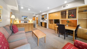 Habitación de hotel con sofá, una pequeña mesa, zona de cocina y mesa de comedor con sillas.