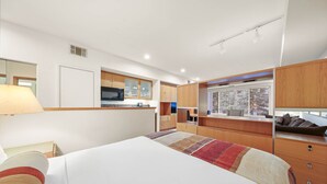 Un dormitorio con cama, escritorio, ventana y kitchenette.