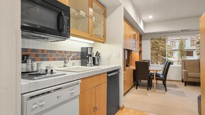 Una cocina compacta con microondas, estufa y cafetera. Hay un comedor con mesa y sillas, y un ventanal con vistas a edificios.