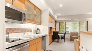 A modern kitchen with stainless steel appliances, a dining area with a table and chairs, and a view through the window.