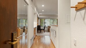 A narrow hallway with wooden flooring, a glass door on the left, and a dining area with a table and chairs on the right.