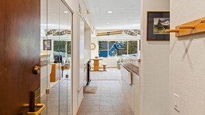 A hallway with a wooden door, glass sliding doors, a view of a blue house, and a framed picture on the wall.