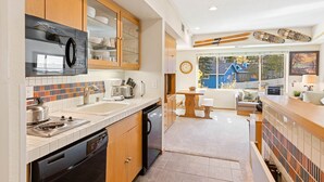 A modern kitchen with wooden cabinets, a built-in microwave, and a large window overlooking a blue house.