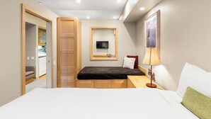 Una habitación de hotel compacta con una cama, un escritorio pequeño, un televisor montado en la pared y una ventana.