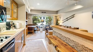A modern kitchen with a wooden countertop, a built-in oven, and a sink. There is a dining area with a table and chairs, and a view of the outside through large windows.