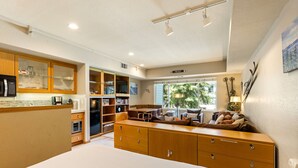 A modern kitchen with wooden cabinets, a dining area, and a large window with a view of greenery.