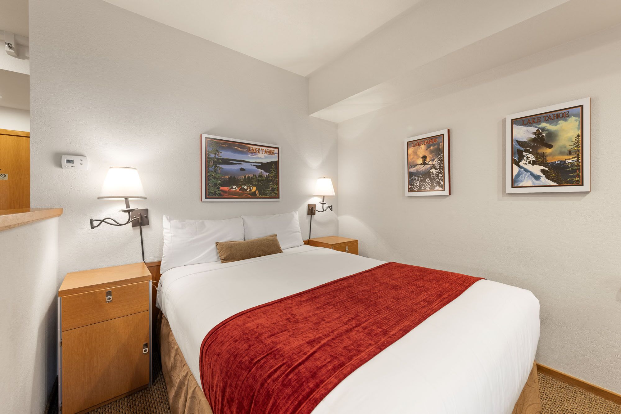 Ein Hotelzimmer mit einem großen Bett, zwei Nachttischen, einer roten Tagesdecke und drei gerahmten Bildern an der Wand.