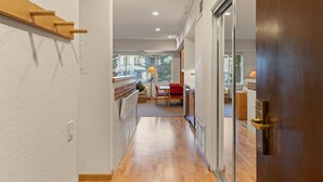 A narrow hallway with wooden flooring and white walls, leading to a dining area with a table and chairs.