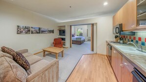 A compact living space with a kitchenette, a sofa, a small table, and a bed in the background.