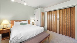 A bedroom with a large bed, two bedside tables with lamps, a wooden wardrobe, and a bench.