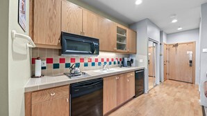 A modern kitchen with wooden cabinets, a stainless steel dishwasher, a microwave, and a tiled backsplash.