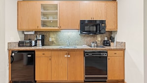 Una cocina compacta con armarios de madera, microondas integrado, cafetera y lavavajillas.