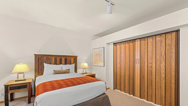 Une chambre à coucher avec une tête de lit en bois, deux tables de chevet avec des lampes, un grand lit avec une jupe de lit marron et une armoire en bois.