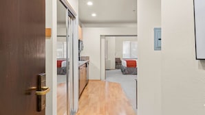 Un pasillo que conduce a un dormitorio con cama, una silla y una pequeña kitchenette.