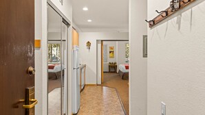Un couloir d’hôtel avec une porte en bois, un réfrigérateur, un lit et une petite table sur laquelle se trouve une plante.