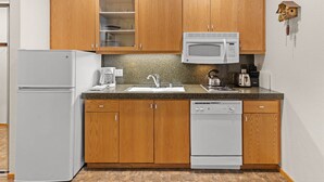 Une cuisine compacte avec des meubles en bois, un réfrigérateur blanc, un four à micro-ondes, une machine à café et un lave-vaisselle.