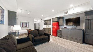A modern living room with a sofa, a dining table, and a kitchen area with a red refrigerator and a TV.