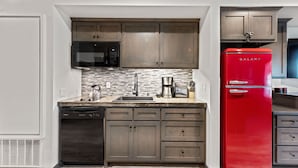 A compact kitchen with wooden cabinets, a black microwave, a red Galanz refrigerator, a coffee maker, and a dishwasher.