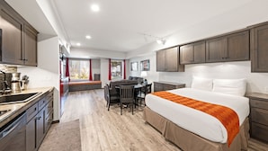 A modern hotel room with a large bed, a dining area, and a kitchen.