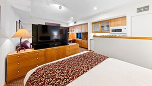 Hotellihuone, jossa on sänky, televisio, puukaapit, mikroaaltouuni ja pieni keittiötila.