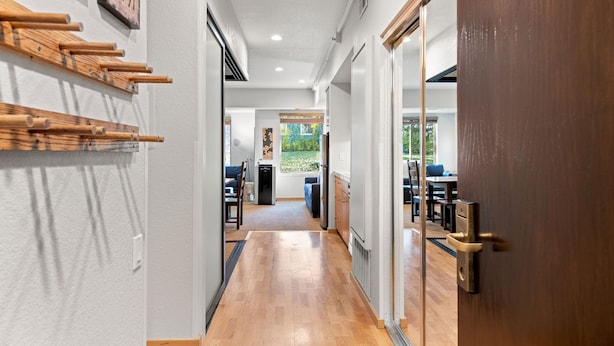 A hallway with wooden slats on the wall, a wooden floor, and a view into a dining area with tables and chairs.