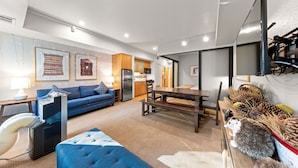 A modern living room with a sofa, a dining table, and a kitchen in the background.