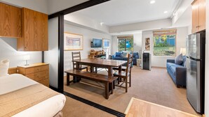A modern living room with a dining area, a kitchen, and a large window offering a view of the outdoors.