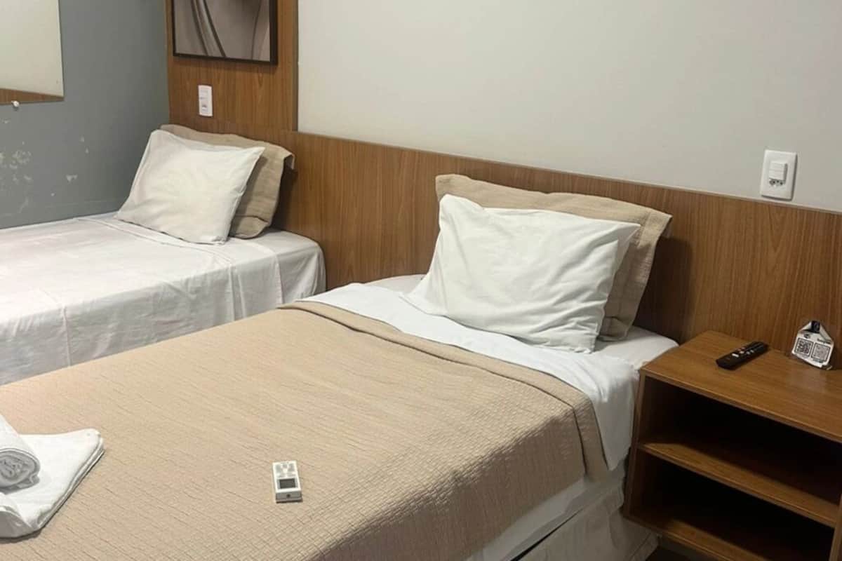 A hotel room with two single beds, a wooden headboard, a bedside table with a remote control, and a wall-mounted mirror.