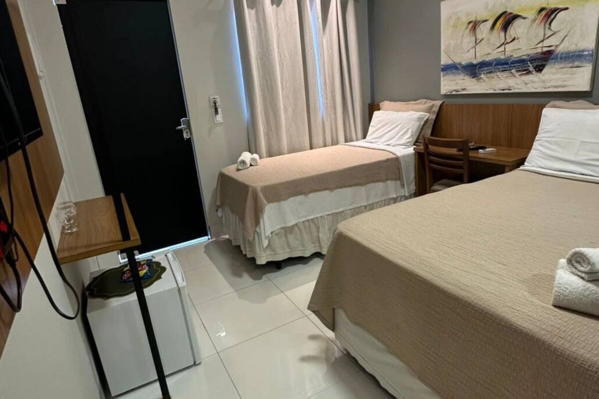 A hotel room with a bed, a desk, a chair, a small table, and a door.