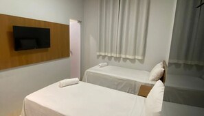 A small, clean room with two single beds, a flat-screen TV mounted on the wall, and a window with curtains. - Hotel Goiano (Estreito)