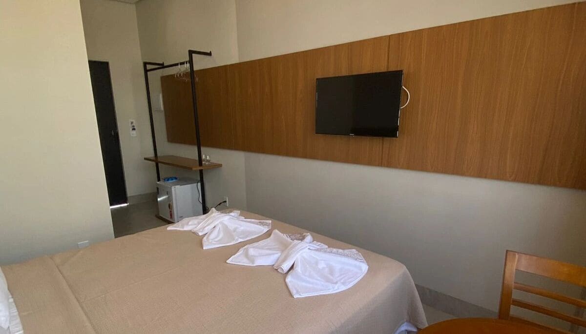 A hotel room with a bed, a television mounted on the wall, and a wooden headboard.