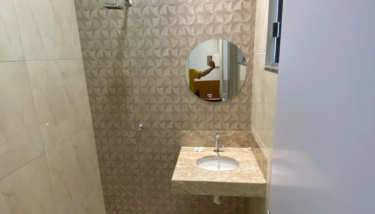 A bathroom with a patterned wall, a round mirror, and a sink with a faucet.