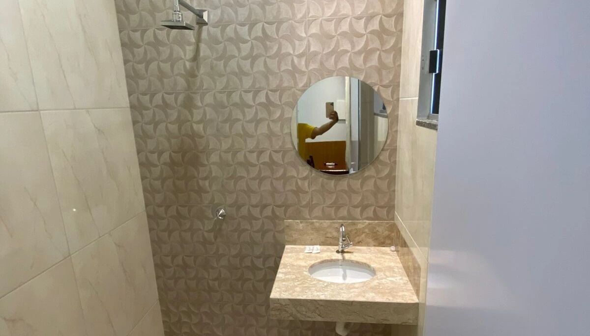 A bathroom with a patterned wall, a round mirror, a sink, and a shower.