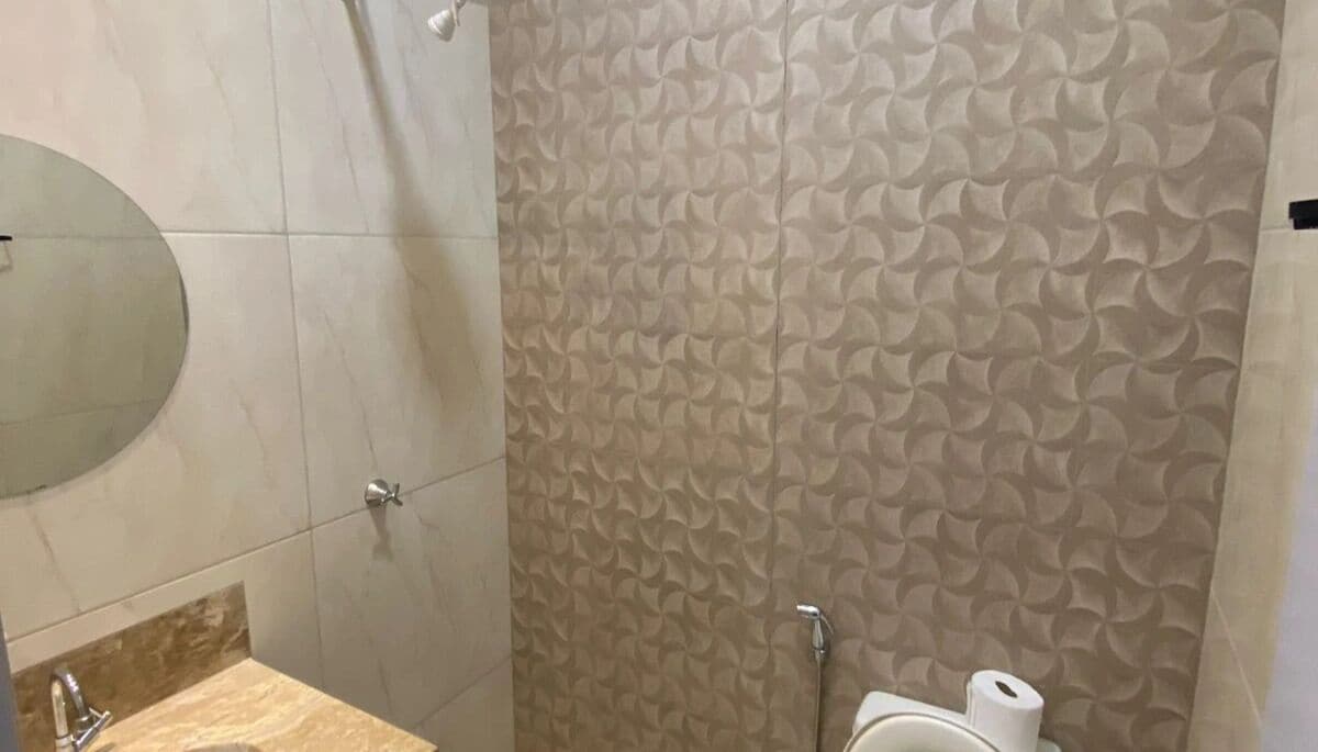 A bathroom with a patterned wall, a round mirror, a toilet, and a shower area.