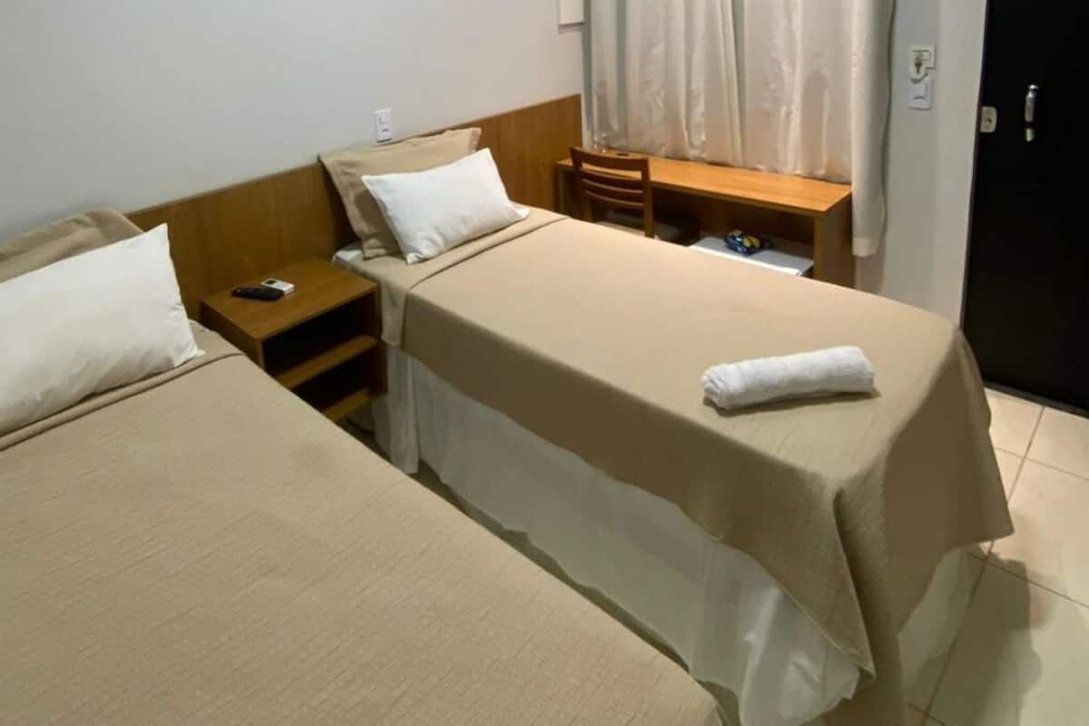A hotel room with two single beds, a wooden nightstand, a small table, and a desk with a chair.