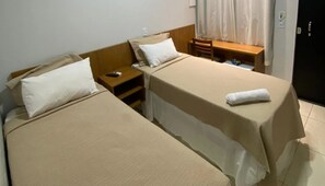 A hotel room with two single beds, a wooden nightstand, a small table, and a desk with a chair. - Hotel Goiano (Estreito)