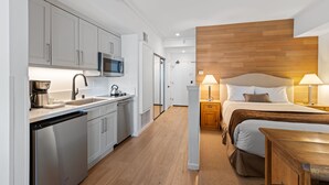 Ein modernes Hotelzimmer mit Küchenzeile, einem Bett mit Holz-Kopfteil und einem Nachttisch mit Lampen.