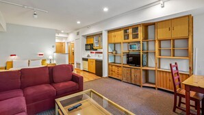 A compact living space with a sofa, a coffee table, a TV, wooden cabinets, and a kitchenette. - 104 | Peaceful Studio - Hot Tubs + Nature Walks (Olympic Valley)