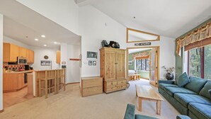 A spacious living area with a sofa, a wooden cabinet, and a kitchen area with wooden cabinets and a microwave.