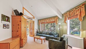 A cozy living room with a wooden cabinet, a sofa, a coffee table, and a large window with curtains.