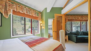 A bedroom with a large bed, a view of the outdoors, and a green sofa in the adjacent room.